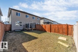 Expansive backyard featuring a stained wood fence, a two-story home with neutral siding, a ground-level deck, and multiple windows - 