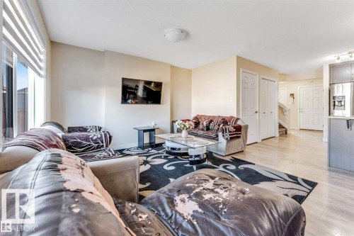 Bright living area featuring light-toned walls, wood-finish flooring, and a large sliding glass door with horizontal blinds - 1715 27 Street, Edmonton, AB 
