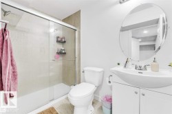 Full bathroom featuring a shower-tub combination with sliding glass doors, neutral-toned shower surround tiling, a white vanity with cabinet storage, a curved basin sink, and a circular wall mirror - 