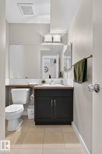 Powder room featuring a single vanity with dark cabinetry, integrated sink, and chrome faucet - 89 9535 217 Street, Edmonton, AB 