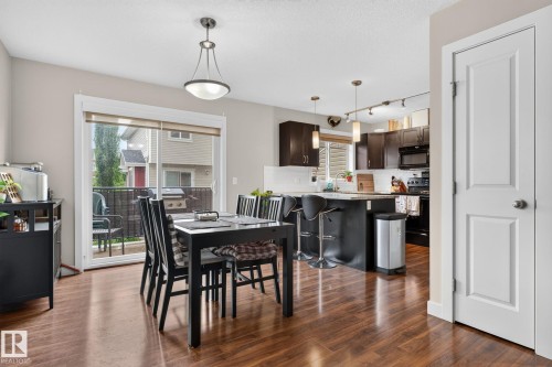 Open-concept dining area featuring wood-finish flooring, a contemporary pendant light fixture, and sliding patio doors - 89 9535 217 Street, Edmonton, AB 
