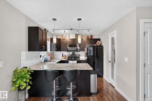 Kitchen featuring dark wood-finish cabinetry, light-toned countertops, a white subway tile backsplash, stainless steel sink, and wood-finish flooring - 89 9535 217 Street, Edmonton, AB 