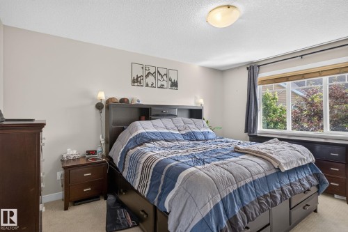 Windowed bedroom featuring neutral wall tones, textured ceiling, and a flush-mount ceiling light - 89 9535 217 Street, Edmonton, AB 