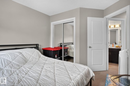 Neutral tone walls and carpeting throughout a bedroom featuring a sliding mirrored closet door and a white paneled door opening to a bathroom with a dark wood-finish vanity - 89 9535 217 Street, Edmonton, AB 