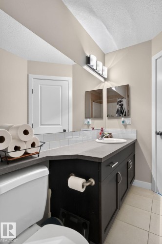 Bathroom featuring a dark wood-finish vanity with a light countertop, a single basin sink, and a large wall-mounted mirror - 89 9535 217 Street, Edmonton, AB 