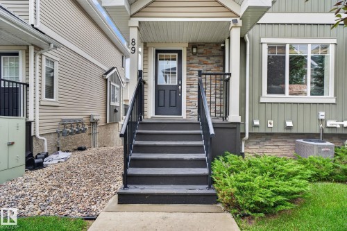 Front entry featuring a dark paneled door, stone facade accents, and a dark railing - 89 9535 217 Street, Edmonton, AB 