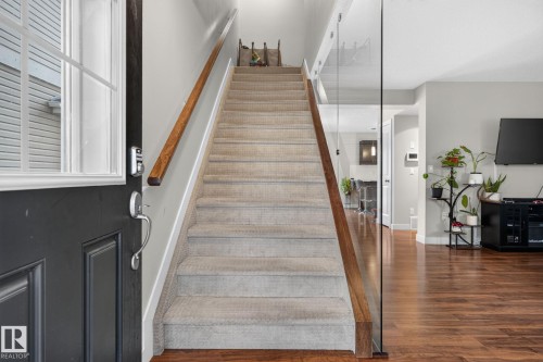 Staircase featuring carpeted treads, wood-finish handrails, and a contemporary glass railing - 89 9535 217 Street, Edmonton, AB 