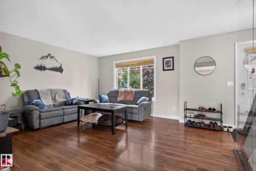 Spacious living area featuring wood-finish flooring, light-toned wall paint, and a large multi-pane window - 89 9535 217 Street, Edmonton, AB 