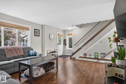 Open concept living area featuring wood-finish flooring, a modern glass staircase railing, and large windows with natural light - 89 9535 217 Street, Edmonton, AB 