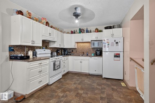 Well-appointed kitchen featuring extensive white cabinetry, a tiled backsplash, and durable patterned flooring - 8316 157 Avenue, Edmonton, AB 