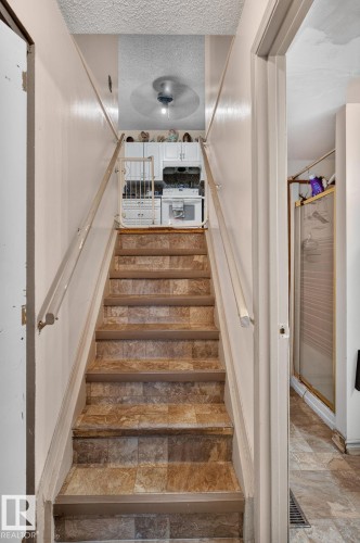 Staircase with patterned flooring, white wall-mounted handrails, and a ceiling fan visible at the landing - 8316 157 Avenue, Edmonton, AB 