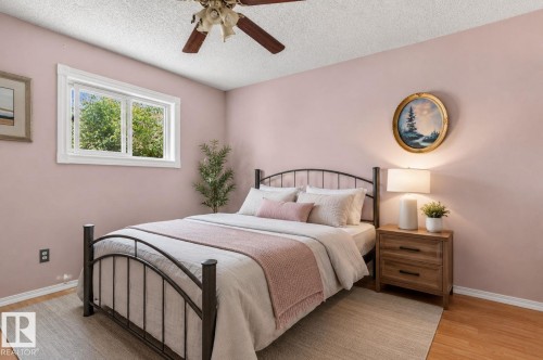 Inviting room featuring a window with white trim, wood-finish flooring, a ceiling fan, and painted walls - 8316 157 Avenue, Edmonton, AB 