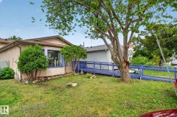 Exterior featuring a prominent accessibility ramp, bay window with blue trim, mature tree, and established landscaping - 