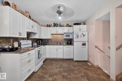 Kitchen featuring white cabinetry, mosaic tile backsplash, brown-toned flooring, and a ceiling fan with integrated lighting - 