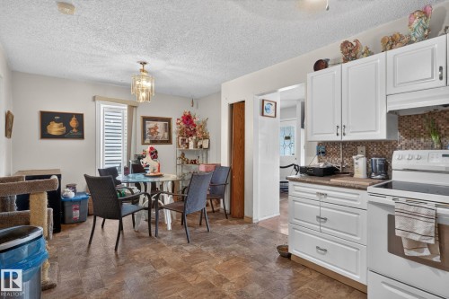 Kitchen and dining area featuring white cabinetry, a mosaic tile backsplash, and a contemporary pendant light fixture - 8316 157 Avenue, Edmonton, AB 