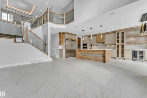 Open-concept living space featuring large format marble-look flooring, a modern kitchen island with pendant lighting, a built-in stainless steel refrigerator, and glass-paneled cabinetry - 2611 62 Avenue, Rural Leduc County, AB - Indoor Photo Showing Other Room