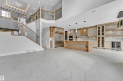 Open-concept living space featuring large format marble-look flooring, a modern kitchen island with pendant lighting, a built-in stainless steel refrigerator, and glass-paneled cabinetry - 