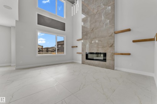 Great room featuring a floor-to-ceiling tiled fireplace with an integrated modern firebox, high ceilings, large windows, recessed lighting, and white marble-look tile flooring - 2611 62 Avenue, Rural Leduc County, AB - Indoor With Fireplace