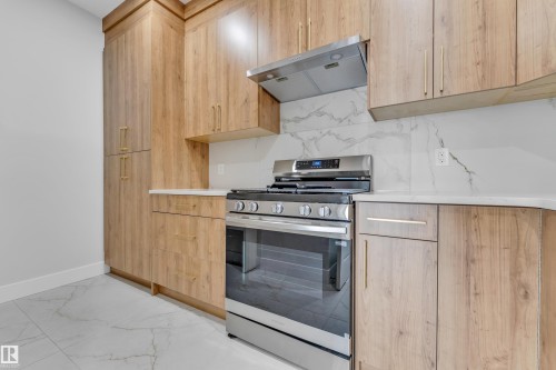 Modern kitchen featuring wood-finish cabinetry, a stainless steel range with overhead hood, white countertops, and a white backsplash with gray veining - 2611 62 Avenue, Rural Leduc County, AB - Indoor Photo Showing Kitchen