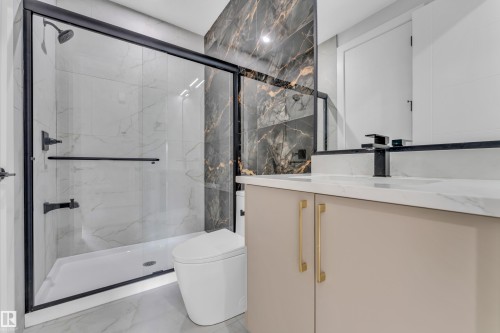 Bathroom featuring a black-framed glass shower enclosure, white marbled tile, a beige vanity with gold-tone hardware, a black faucet, and a black and gold marbled accent wall - 2611 62 Avenue, Rural Leduc County, AB - Indoor Photo Showing Bathroom