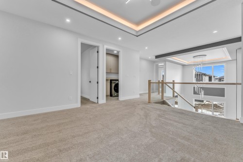 Carpeted upper level featuring a glass and wood railing system, tray ceiling with recessed lighting, laundry area with built-in cabinetry, and a tiered chandelier - 2611 62 Avenue, Rural Leduc County, AB - Indoor Photo Showing Other Room