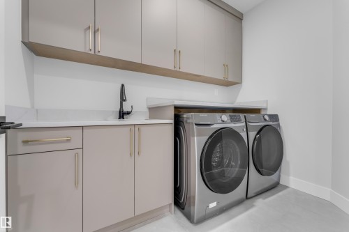Laundry area featuring light gray cabinetry with gold-toned hardware, white solid surface countertops, and a black gooseneck faucet - 2611 62 Avenue, Rural Leduc County, AB - Indoor Photo Showing Laundry Room