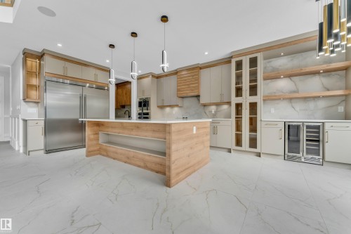 Contemporary kitchen featuring a large central island, integrated stainless steel appliances, extensive cabinetry with glass accents, open wood-finish shelving, and a beverage cooler - 2611 62 Avenue, Rural Leduc County, AB - Indoor Photo Showing Kitchen With Upgraded Kitchen