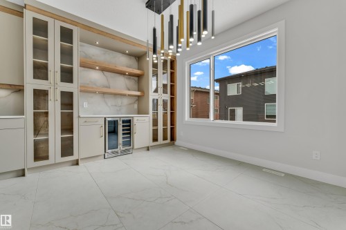 Built-in cabinetry with glass-front uppers and a beverage cooler, complemented by a large window with white trim, marble-look tile flooring, and a contemporary multi-pendant lighting fixture - 2611 62 Avenue, Rural Leduc County, AB - Indoor Photo Showing Other Room
