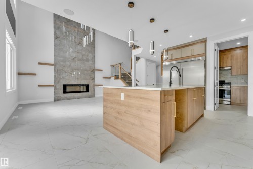 Spacious open-concept interior featuring a floor-to-ceiling tiled fireplace surround with an electric insert, a kitchen island with a white countertop and wood-finish cabinetry, sleek pendant lighting, and large format tile flooring - 2611 62 Avenue, Rural Leduc County, AB - Indoor Photo Showing Kitchen With Fireplace With Upgraded Kitchen