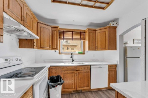 Kitchen featuring wood cabinetry, white countertops, built-in dishwasher, white range, and a window with blinds - 14530 37 Street, Edmonton, AB 