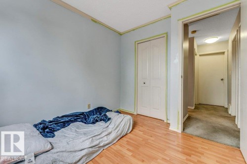 Bedroom space featuring wood-finish flooring, light blue wall paint, a built-in bi-fold closet, and textured ceiling - 14530 37 Street, Edmonton, AB 