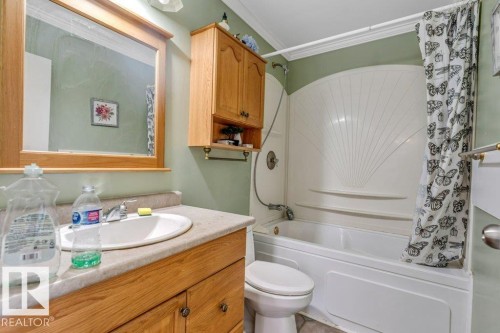 Bathroom featuring a built-in tub/shower combination, a vanity with a drop-in sink, and wood cabinetry - 14530 37 Street, Edmonton, AB 