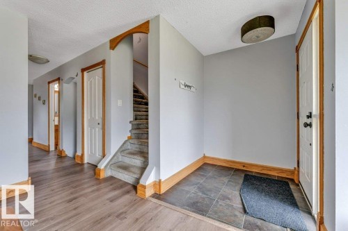 Entryway featuring durable tile flooring, a wood-finish flooring hallway, light grey wall paint, and a carpeted staircase with wood archway accents - 14530 37 Street, Edmonton, AB 