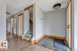 Entryway featuring durable tile flooring, a wood-finish flooring hallway, light grey wall paint, and a carpeted staircase with wood archway accents - 