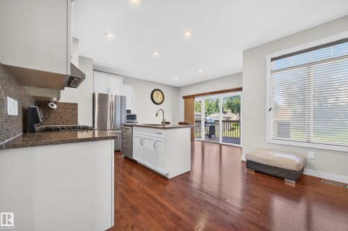 Open-concept kitchen with wood-finish flooring, white cabinetry, dark stone countertops, and a full stainless steel appliance package - 1512 Cunningham Cape, Edmonton, AB 