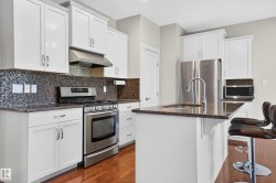 Modern kitchen featuring white cabinetry, stainless steel appliances, a mosaic tile backsplash, and a breakfast bar with stone-finish countertops - 