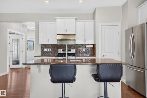 Kitchen featuring a central island with a stone-finish countertop, white cabinetry, a mosaic tile backsplash, and stainless steel appliances - 1512 Cunningham Cape, Edmonton, AB 