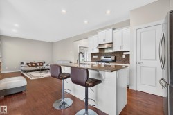 Open-concept kitchen featuring white cabinetry, granite countertops, and a mosaic tile backsplash - 
