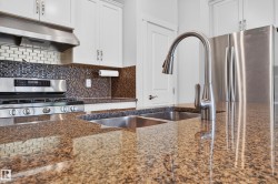 Kitchen featuring granite countertops, stainless steel appliances, a double basin sink, white cabinetry, and varied tile backsplashes - 