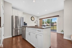 Kitchen island with integrated sink and chrome faucet, granite-style countertop, white cabinetry, and stainless steel appliances - 