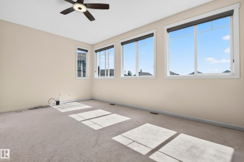 Spacious room featuring multiple large windows, neutral-toned walls, and soft carpeting - 1512 Cunningham Cape, Edmonton, AB 