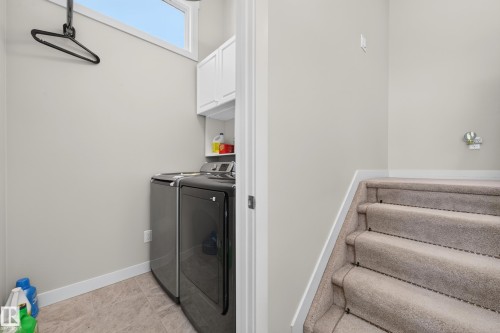 Dedicated laundry area featuring a front-loading washer and dryer, upper cabinetry, and tile flooring - 1512 Cunningham Cape, Edmonton, AB 