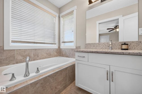 Integrated bathtub with deck-mounted chrome fixtures, surrounded by neutral-toned tiled walls - 1512 Cunningham Cape, Edmonton, AB 