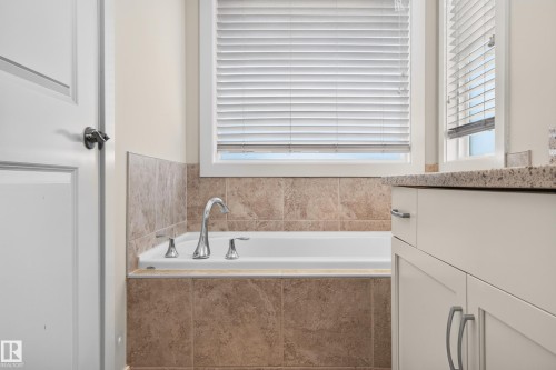 Built-in soaking tub with chrome fixtures, surrounded by neutral-toned tile - 1512 Cunningham Cape, Edmonton, AB 