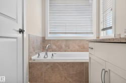 Built-in soaking tub with chrome fixtures, surrounded by neutral-toned tile - 