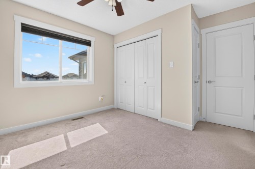 Carpeted room featuring a ceiling fan with light, white trim, a large window with a roller shade, and two white panel doors - 1512 Cunningham Cape, Edmonton, AB 
