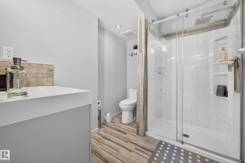 Tiled shower enclosure with glass sliding door and built-in shelving, complemented by wood-finish flooring - 1512 Cunningham Cape, Edmonton, AB 