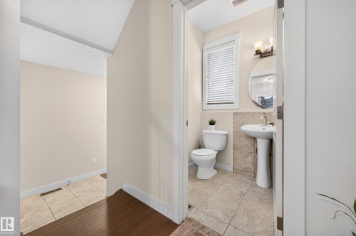 Bathroom featuring a pedestal sink with a single-handle faucet, circular mirror, and tile flooring - 1512 Cunningham Cape, Edmonton, AB 