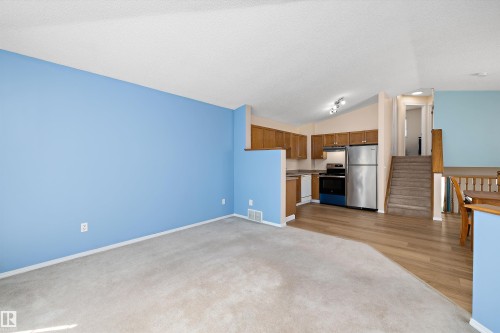Open-concept living space featuring carpeted flooring and a bright blue accent wall - 15016 134 Street, Edmonton, AB 