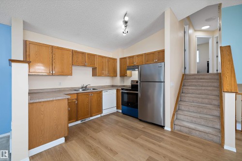 Kitchen featuring wood-finish cabinetry, stainless steel refrigerator and range, a white dishwasher, and light-toned countertops - 15016 134 Street, Edmonton, AB 